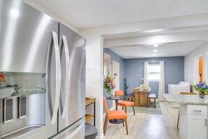Egy modern konyha rozsdamentes acélból készült berendezésekkel, egy étkező rész narancssárga székekkel, és egy kis asztallal, melyen egy virágváz áll.
