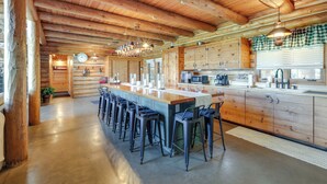 A spacious kitchen with a long island, bar stools, wooden cabinets, and a hanging light fixture.