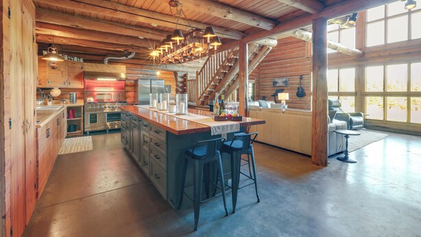 A spacious kitchen with a large island, wooden ceiling beams, and a staircase leading to an upper level.