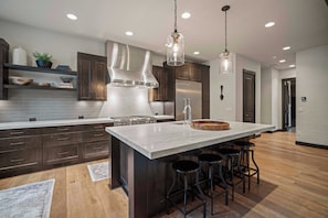 Una cocina moderna con alacenas de madera oscura, una isla grande con taburetes, electrodomésticos de acero inoxidable e iluminación colgante.