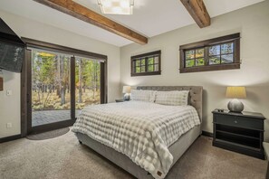 A bedroom with a large bed, two windows, a TV, and a nightstand with a lamp. - Forest View Hideaway with Access to Forest House (Sunriver)