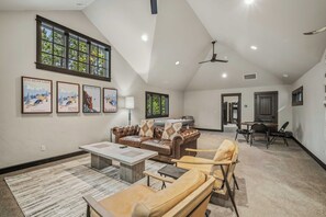 A spacious living room with a high ceiling, a large window, and a fireplace. There are multiple seating options including a sofa and chairs. - Forest View Hideaway with Access to Forest House (Sunriver)