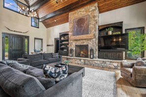 A spacious living room with a stone fireplace, comfortable seating, and a large TV.