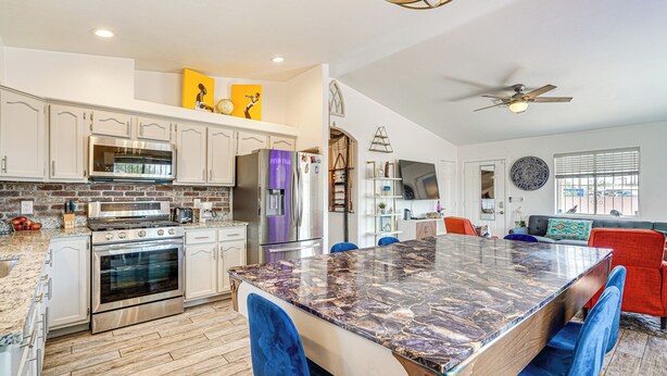 A modern kitchen with stainless steel appliances, a marble island, and blue chairs. - Tucson Retreat w/ Fire Pit: 4 Mi to Downtown! (Tucson)