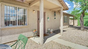 A house with a covered porch, a small table with a chair, and a bird perched on the window sill. - Tucson Retreat w/ Fire Pit: 4 Mi to Downtown! (Tucson)
