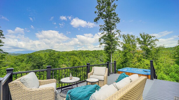 Une terrasse dotée de meubles en osier, d’un jacuzzi et offrant une vue panoramique sur une zone boisée.