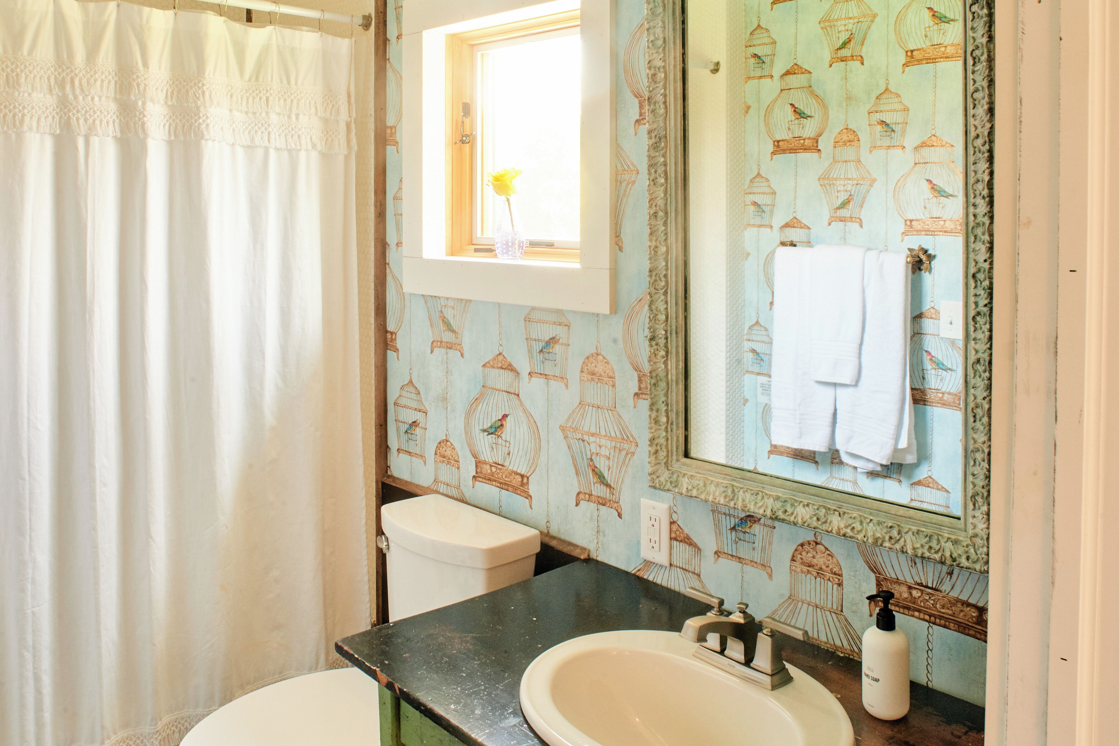 Een badkamer met een wit toilet, een wastafel met een zwarte aanvoegtop en een spiegel met behangpapier met een vogelmotief.