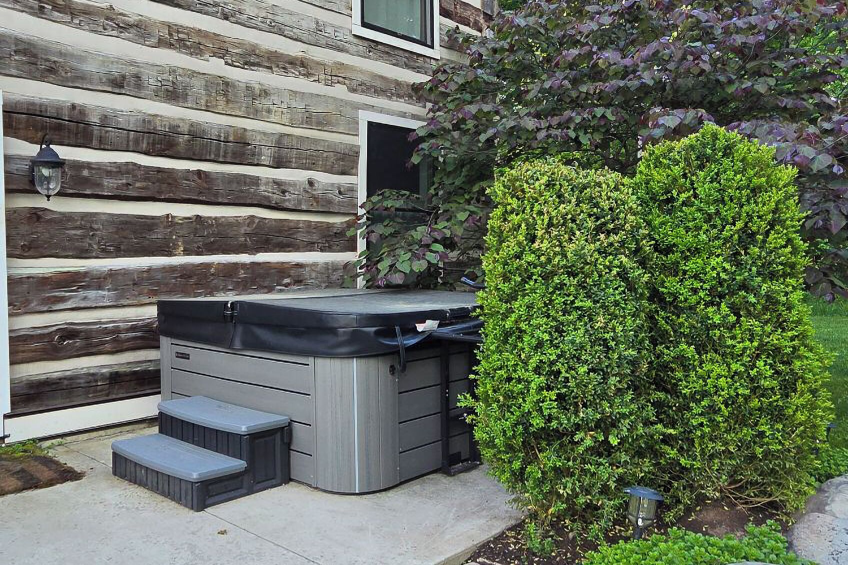 A hot tub with steps, a wooden exterior wall, and a well-maintained hedge.