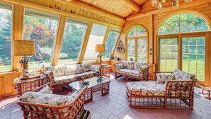 A cozy wooden interior with large arched windows, wicker furniture, and a ceiling with wooden beams and hanging lights. - Pond & Hot Tub! Airy Hudson Valley Escape (Austerlitz)