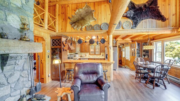 A rustic interior with a stone fireplace, leather armchair, dining area, and wooden beams. - Pond & Hot Tub! Airy Hudson Valley Escape (Austerlitz)