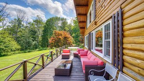 A wooden deck with outdoor seating, a wooden cabin, and a view of a forest. - Pond & Hot Tub! Airy Hudson Valley Escape (Austerlitz)