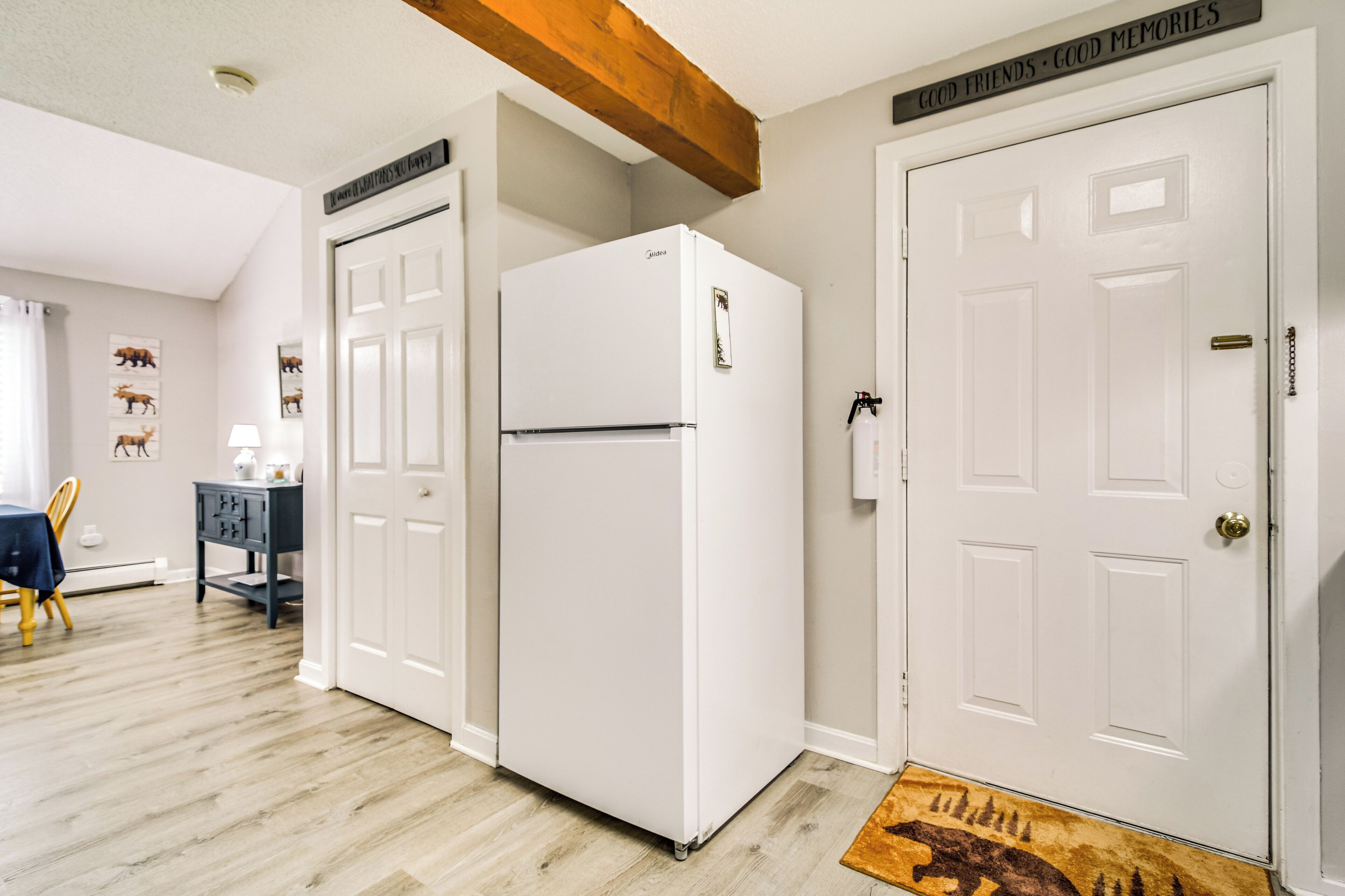 Une cuisine avec un réfrigérateur blanc, un plancher en bois et une porte ornée d’une inscription : « Bons amis, bons souvenirs ».