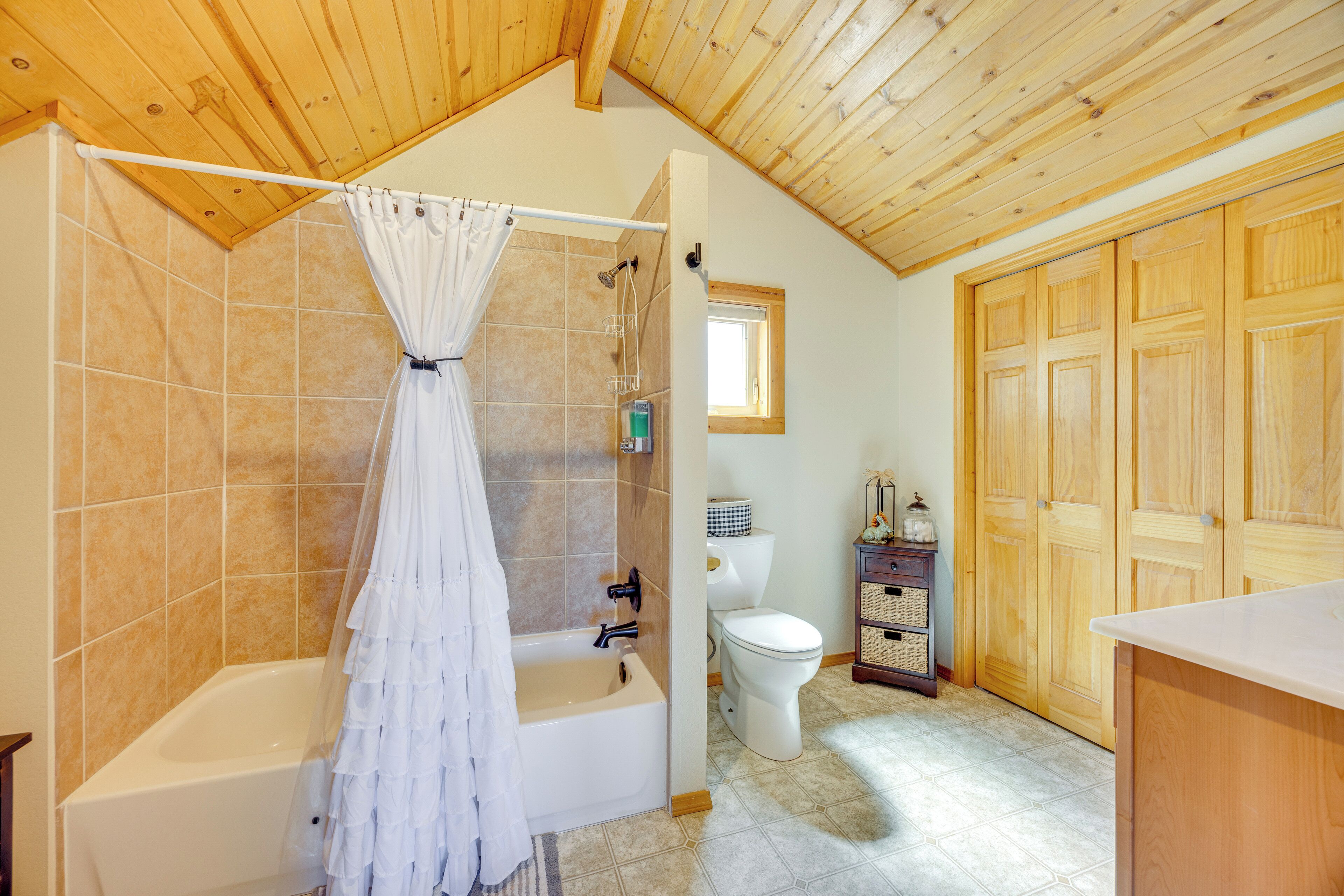A bathroom with a bathtub, shower, and toilet, wooden ceiling, and tiled walls.