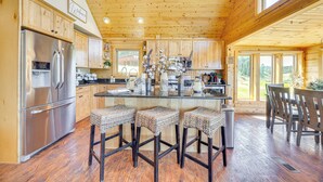 A spacious kitchen with wooden cabinets, a stainless steel refrigerator, and a central island with bar stools. - Lakefront Divide Cabin w/ Game Room! (Woodland Park)