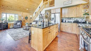 A spacious kitchen with wooden cabinets, a central island, and a stainless steel refrigerator. - Lakefront Divide Cabin w/ Game Room! (Woodland Park)