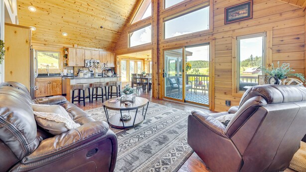A spacious living area with leather sofas, a coffee table, and a large window offering a view of the outdoors. - Lakefront Divide Cabin w/ Game Room! (Woodland Park)