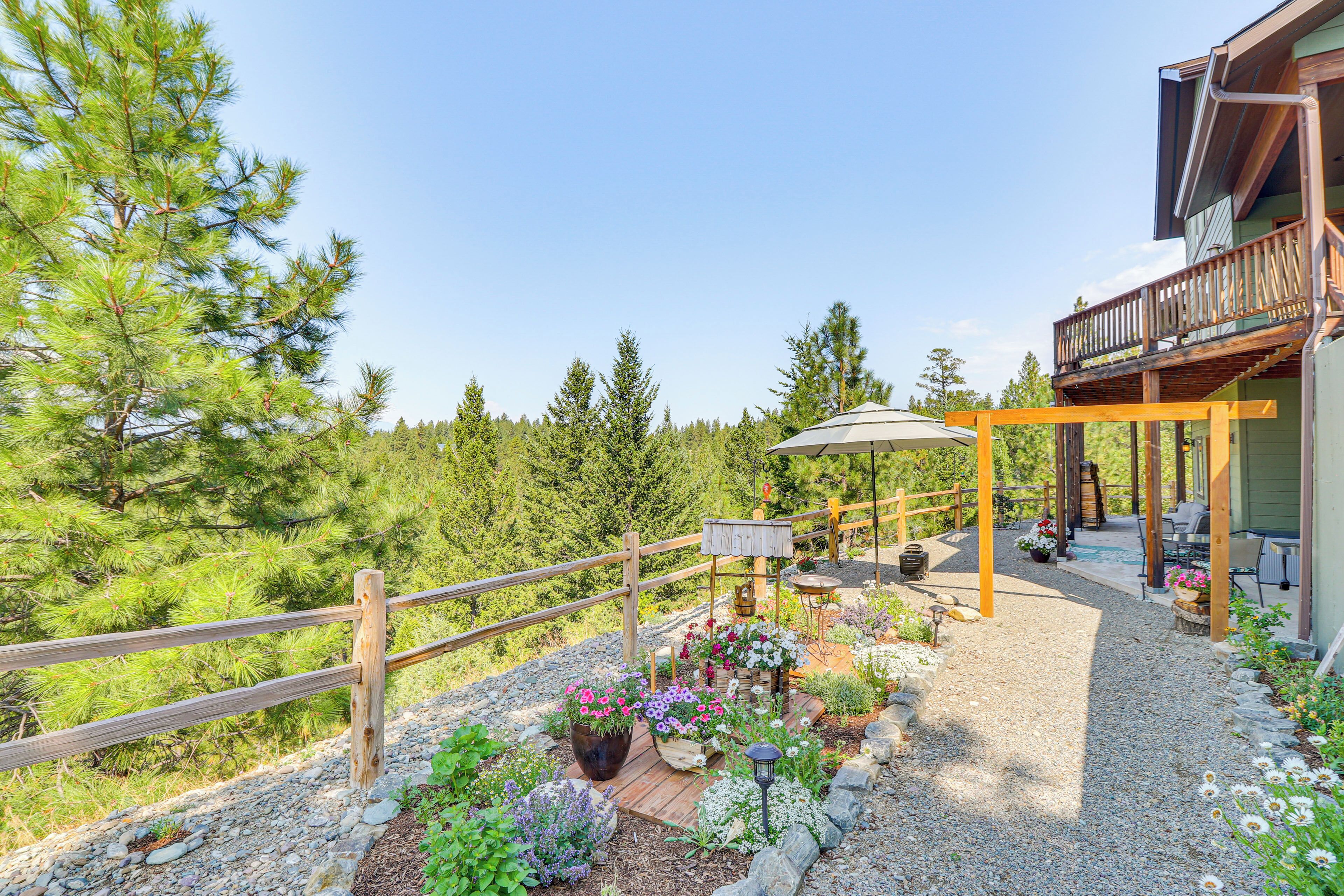 Eine Holzterrasse mit einer Pergola, umgeben von einem Kiesweg und Blumenbeeten.