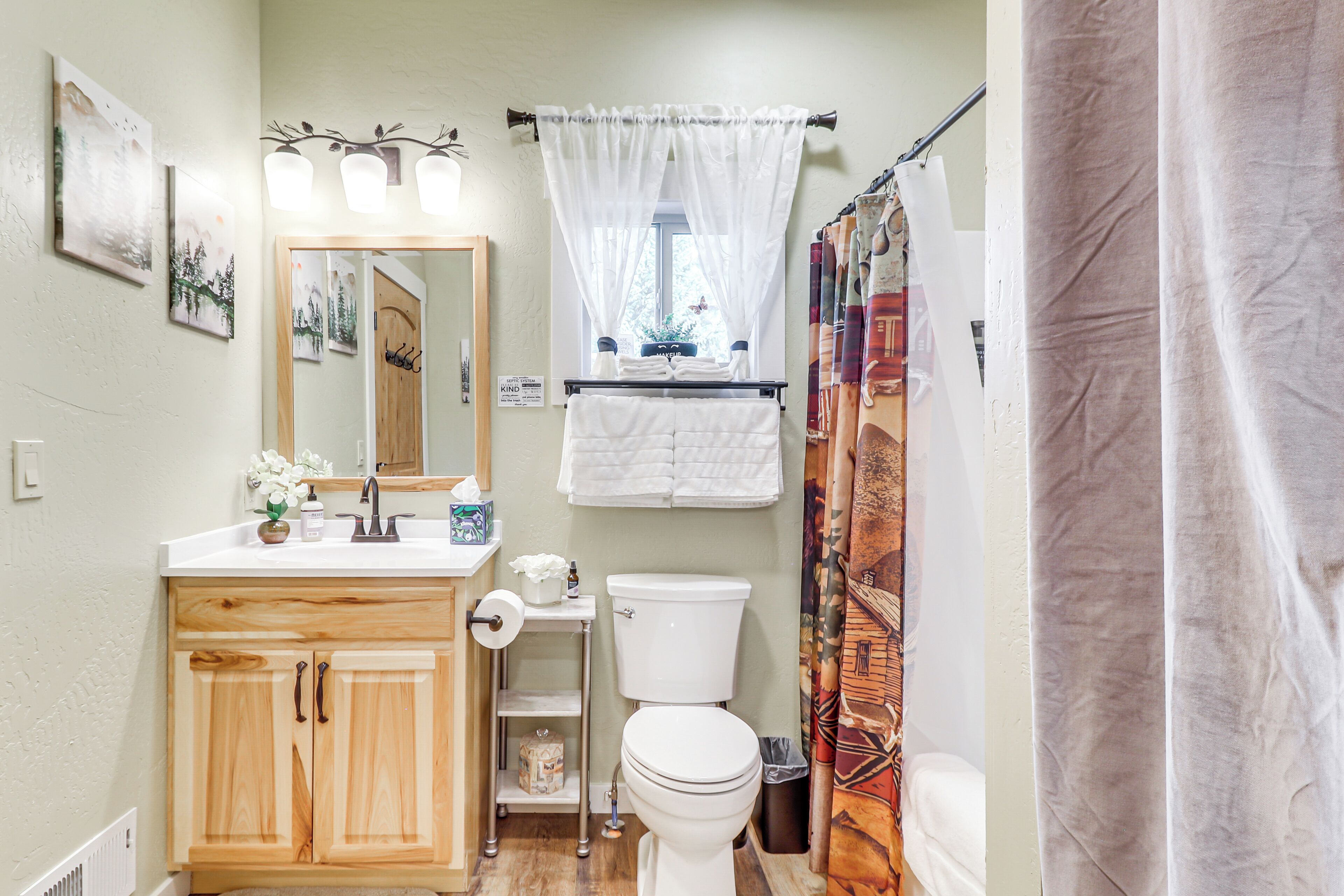 Une salle de bain avec des meubles en bois, des toilettes blanches, un lavabo avec un miroir et un rideau de douche.