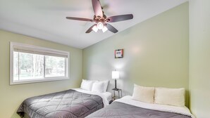 A bedroom with two beds, a ceiling fan, a bedside table with a lamp, and a window with blinds.