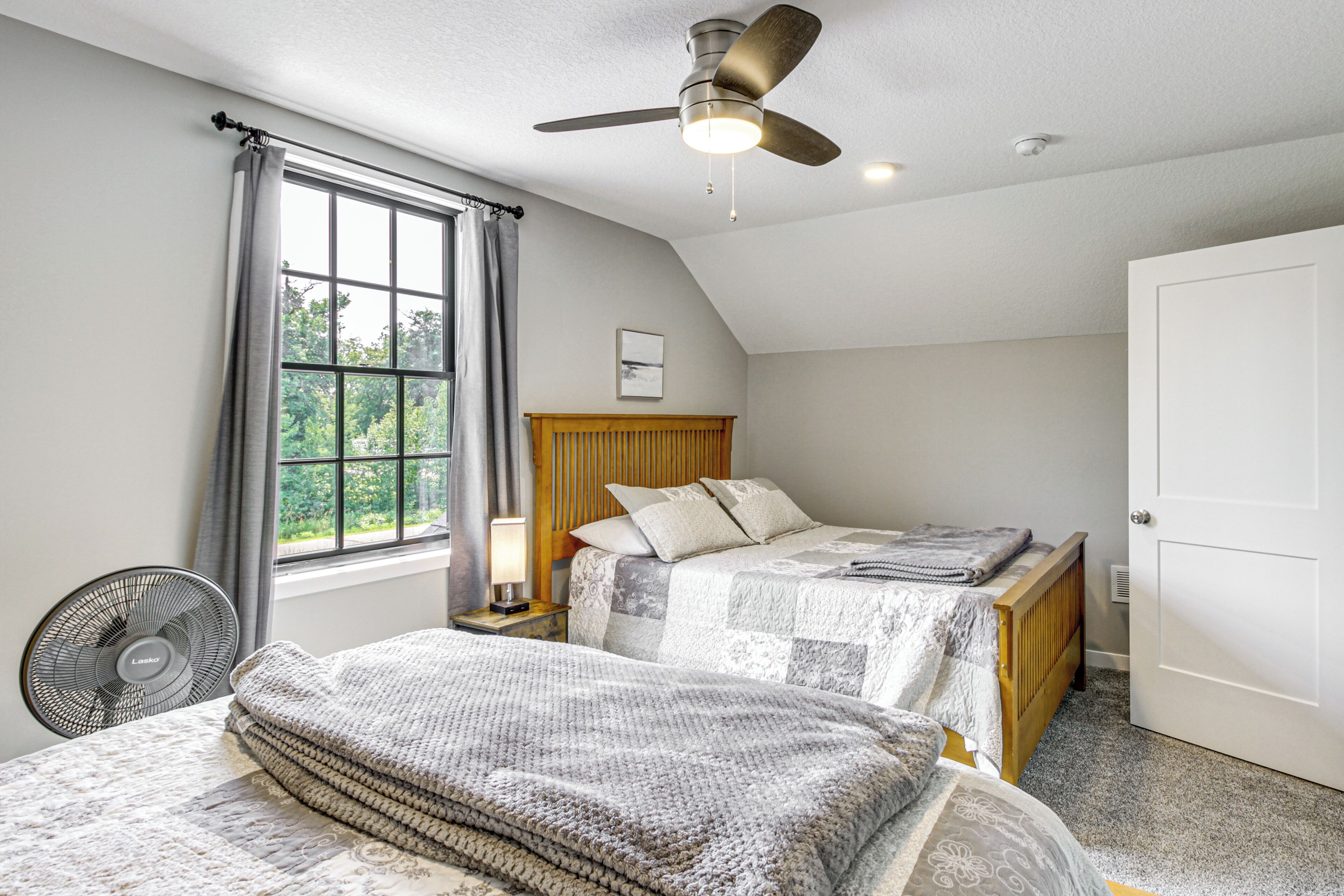 A bedroom with two beds, a ceiling fan, a window with curtains, and a door.