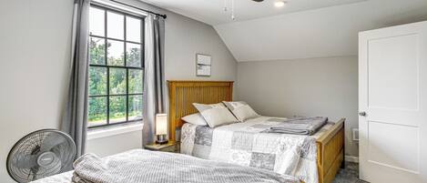 A bedroom with two beds, a ceiling fan, a window with curtains, and a door.