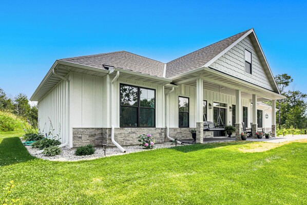 A two-story house with a covered porch, stone foundation, and a well-maintained lawn.