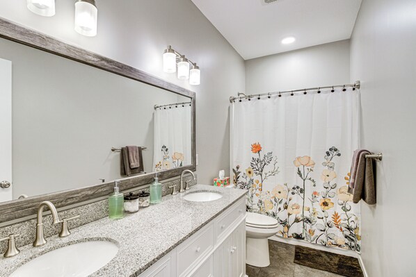 A bathroom with two sinks, a large mirror, and a shower curtain with floral patterns. - Onamia Vacation Rental ~ 1 Mi to Mille Lacs Lake! (Onamia)