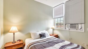 Une chambre à coucher avec un lit, deux tables de chevet, une lampe et une fenêtre avec des stores.