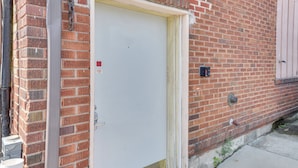 Une porte blanche fermée avec une poignée en métal, un mur de briques et une plaque de métal avec un cadenas.