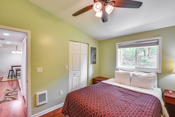 A bedroom with a bed, a ceiling fan, a window with blinds, and a door.