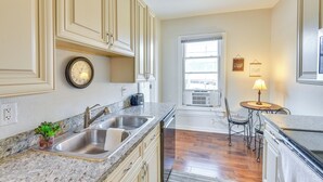 A kitchen with a sink, countertop, cabinets, and a clock. There is a window with a view of the outside. - 2 Mi to Warren Dunes - Bright Sawyer Apartment! (Sawyer)