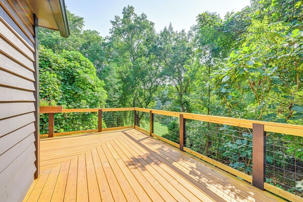 A wooden deck with a metal railing, surrounded by dense green foliage. - Cabin w/ Fire Pit - 7 Mi to Downtown Carrollton! (Carrollton)