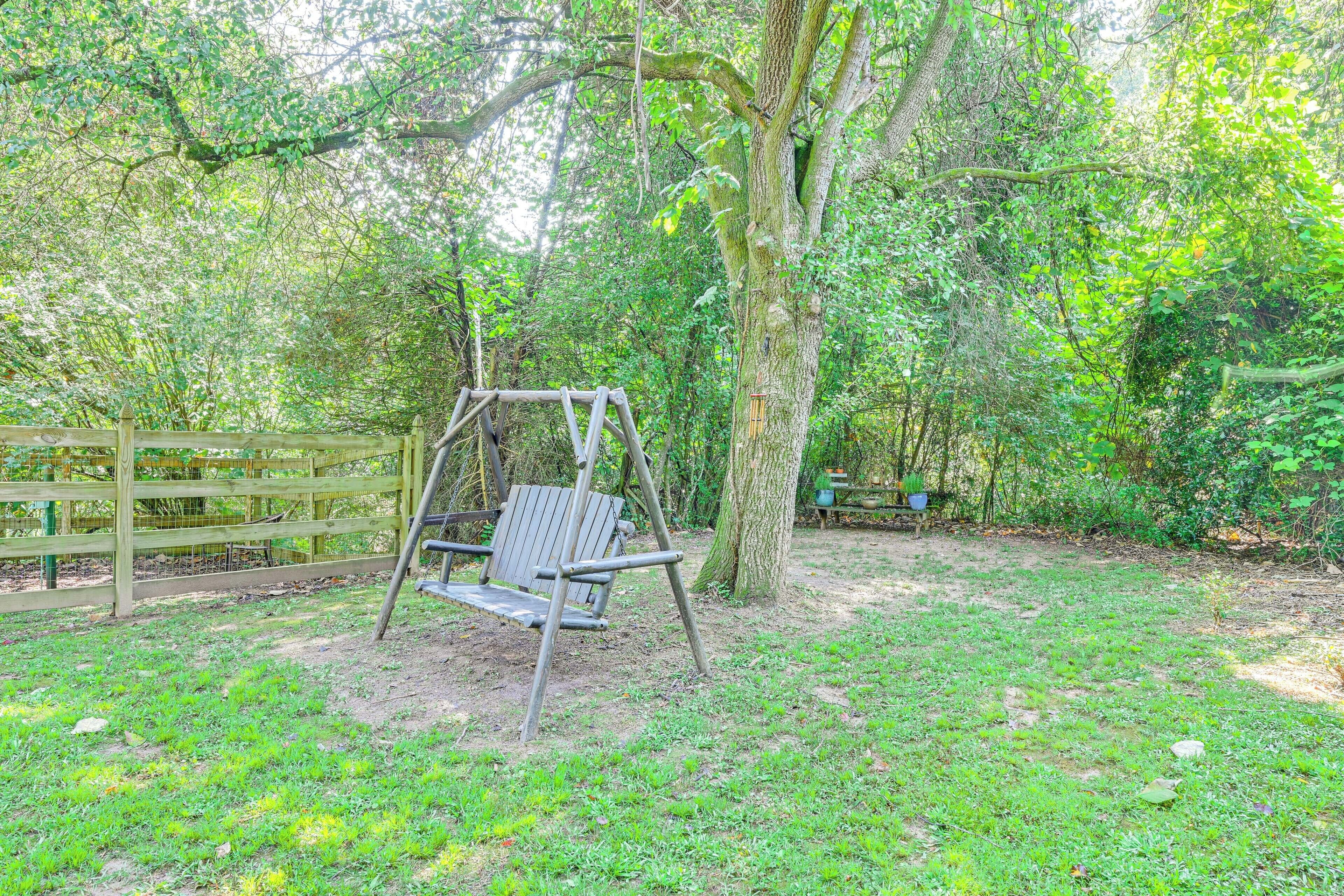 A swing set in a wooded area with a wooden fence and a bench.