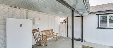 A covered outdoor area with a white refrigerator, a wooden bench, and a rocking chair.