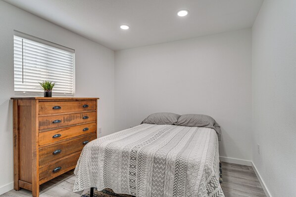 A bedroom with a wooden dresser, a bed with a patterned bedspread, and a window with blinds. - Pet-friendly Home < 1 Mi to Downtown Moses Lake! (Moses Lake)