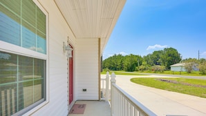 A covered porch with a white railing, a red door, and a clear view of a suburban street with houses and greenery. - 3 Mi to Brunswick Community College: Cozy Duplex! (Bolivia)