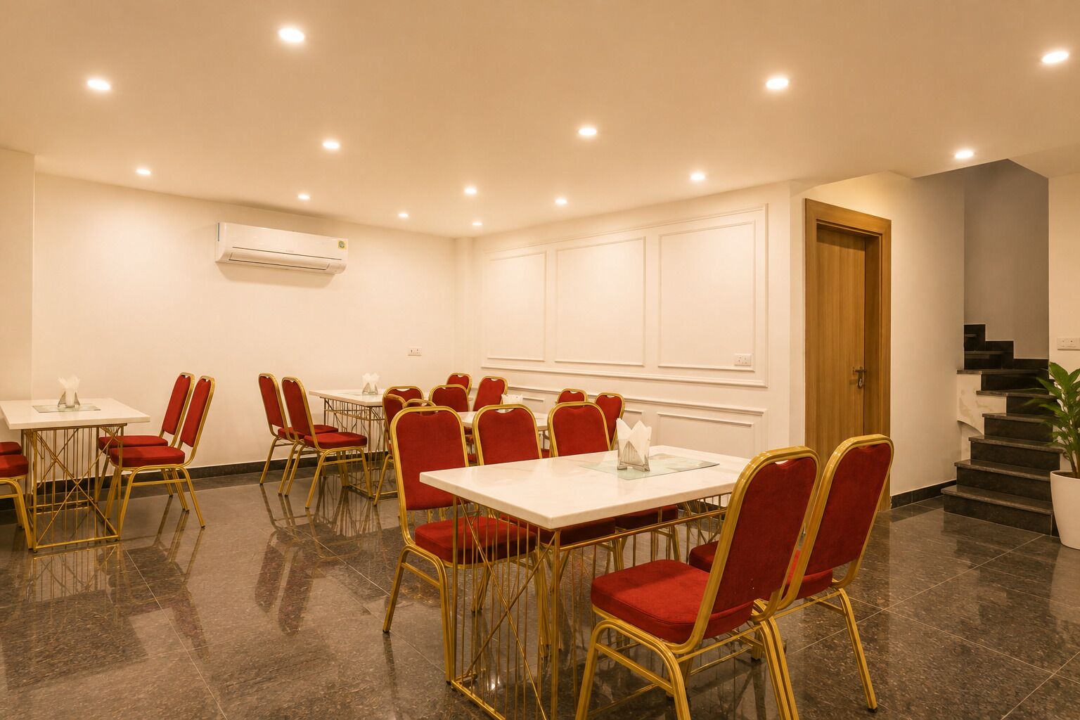 A conference room with tables and chairs, a staircase, and an air conditioning unit on the wall.