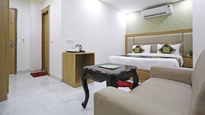 Habitación de hotel con cama, mesita de noche, una silla, una pequeña mesa y un equipo de aire acondicionado.