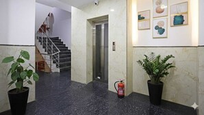 Vestíbulo de hotel con piso de mármol, una escalera, extintor y arte en las paredes.