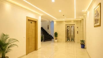 A hotel lobby with a marble floor, a wooden door, a staircase, and a potted plant.