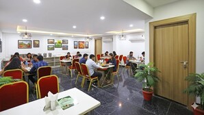 A dining area with multiple tables and chairs, people dining, and wall-mounted artwork. - Hotel Decent Suites - Delhi Airport (New Delhi)
