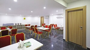 Un salón de conferencias con sillas rojas y doradas, mesas blancas y una puerta de madera.
