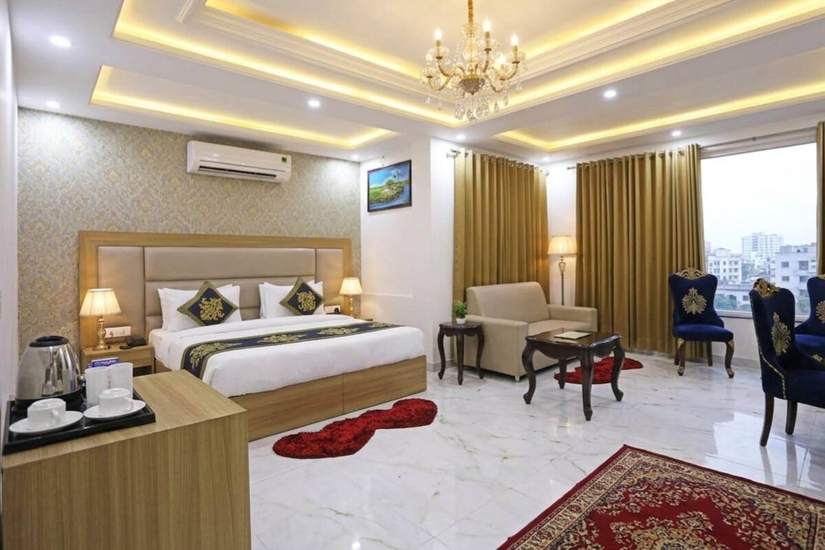 A hotel room with a bed, a desk, a chair, a sofa, a chandelier, and a view of the city.
