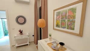Une chambre moderne avec une commode blanche, une œuvre d’art florale encadrée, un luminaire suspendu et une petite plante en pot.
