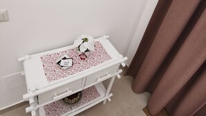 Une salle de bain avec un meuble-lavabo blanc, un miroir rond orné de motifs noirs en forme de pointes et une orchidée en pot.