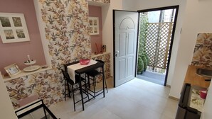 Une cuisine compacte avec un coin repas, dotée d’un sol carrelé blanc, d’une table avec des chaises et d’une porte donnant sur un balcon.