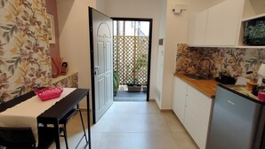 Une cuisine étroite avec des meubles blancs, un plan de travail en bois et un réfrigérateur. Une table à manger avec des chaises est placée au premier plan.