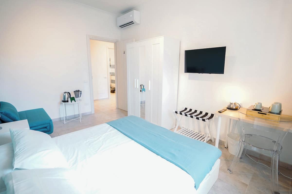 A hotel room with a bed, a desk, a chair, a TV, and a bathroom.