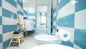 Une salle de bain moderne avec un lavabo blanc, une baignoire et un espace douche. On y trouve une échelle en bois et un petit marchepied près du lavabo.