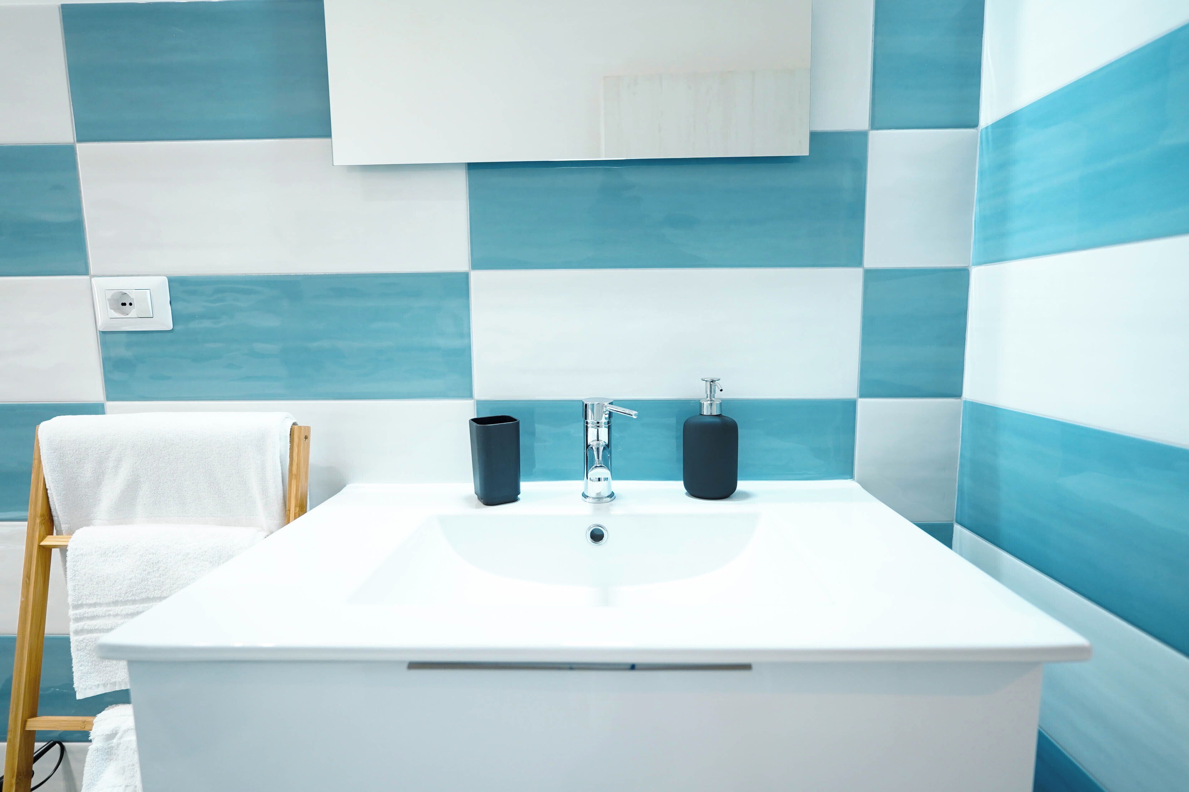 A bathroom with a white sink, two black soap dispensers, and a wooden towel rack with a white towel.